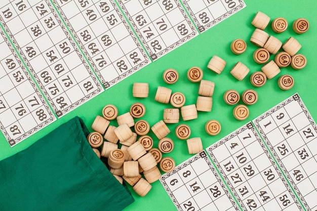 Wooden lotto barrels with cloth bag and game cards on green background