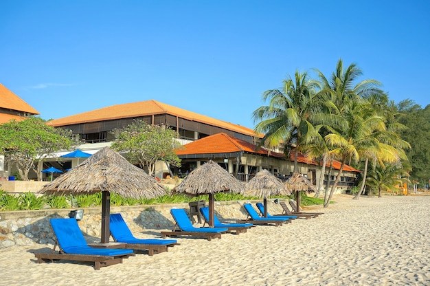 Wooden lounge / deck chairs and umbrella on paradise beach looking out to ocean, blue sky