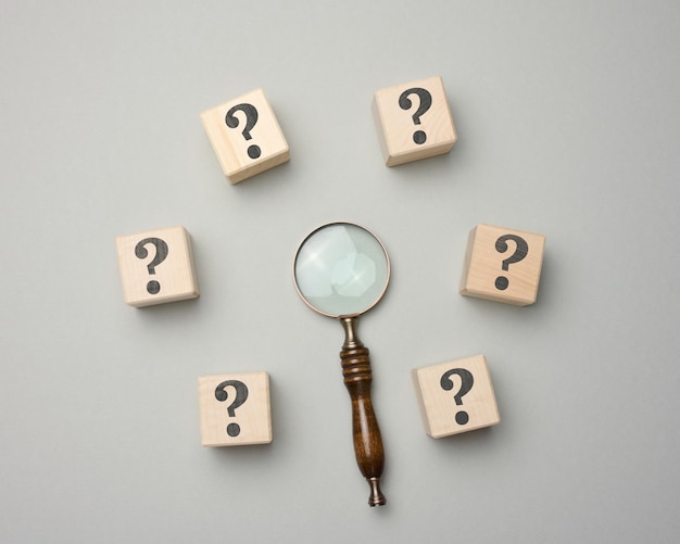 Wooden magnifier and cubes with question marks on gray background