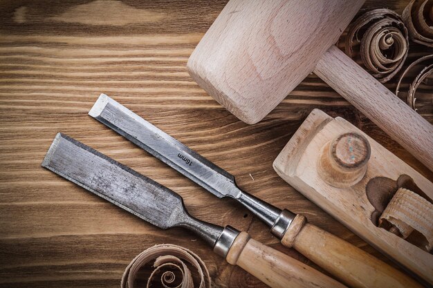 Wooden mallet planer flat chisels curled shavings on vintage wood board construction concept