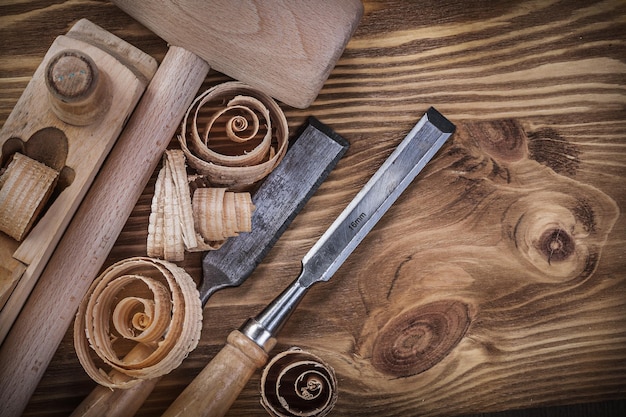 Wooden mallet shaving plane flat chisels curled shavings on vintage wood board construction concept.