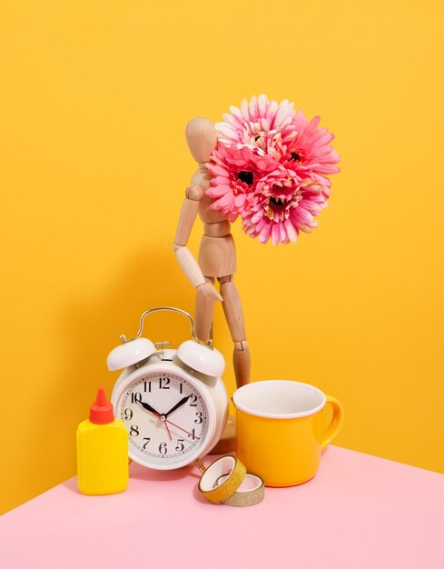 Wooden man holding flowers Retro alarm clock colored ribbons glue and a brightly colored cup