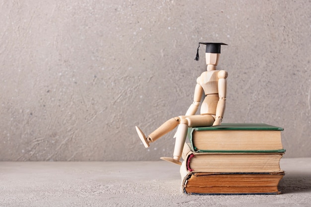 wooden man in a student hat is sitting on books