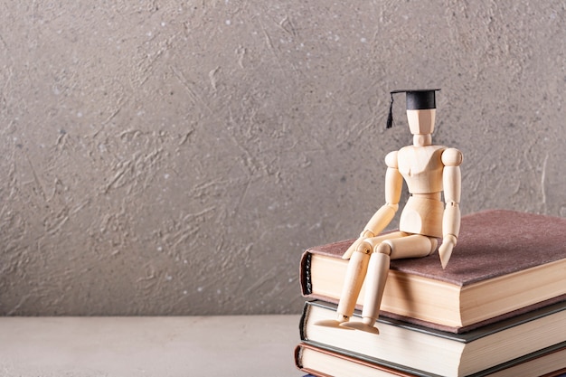 Photo wooden man in a students hat is sitting on books