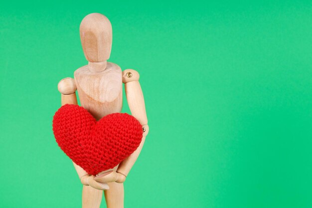 Wooden man with a red heart in his hands on a green background High quality photo