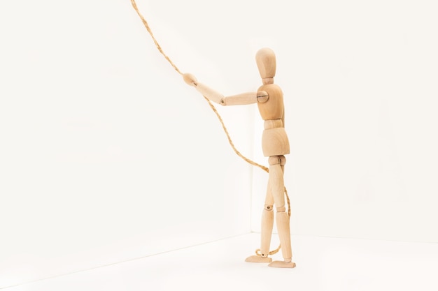 A wooden manequin toy holding holding a thin rope in his hand