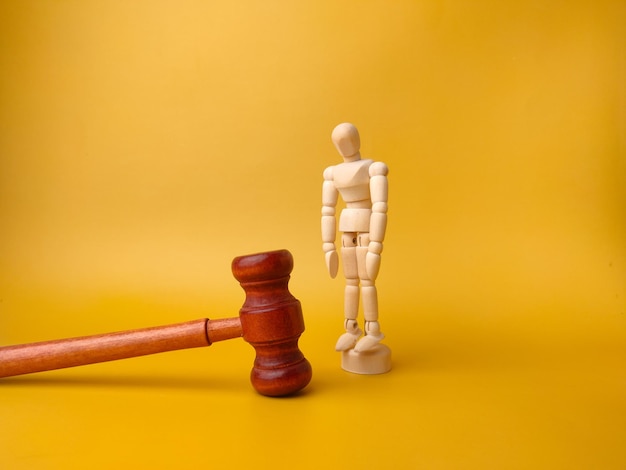 Wooden mannequin and gavel on a yellow background Law concept