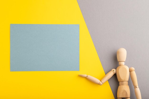 Wooden mannequin holding blue blank poster on gray and yellow pastel background copy space