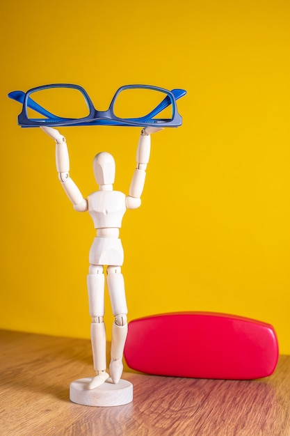 wooden mannequin holding blue glasses on yellow