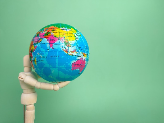 Wooden mannequin holding earth globe on a green background with copy space