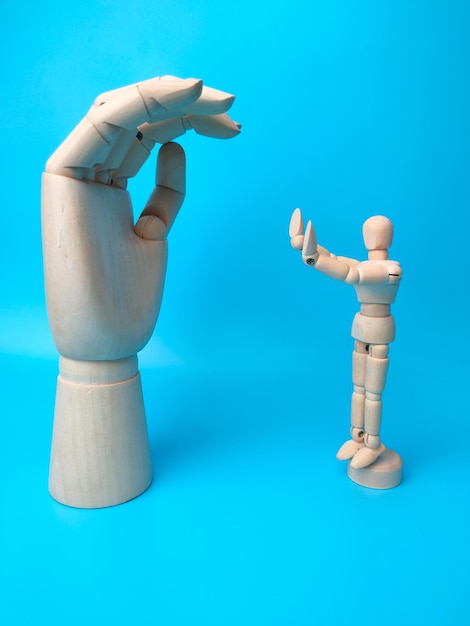 A wooden mannequin makes a stunt holding a wooden hand on a blue background