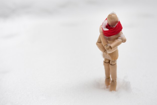 Wooden mannequin in red scarf standing in snowdrift and freezing. Loneliness and winter fashion concept