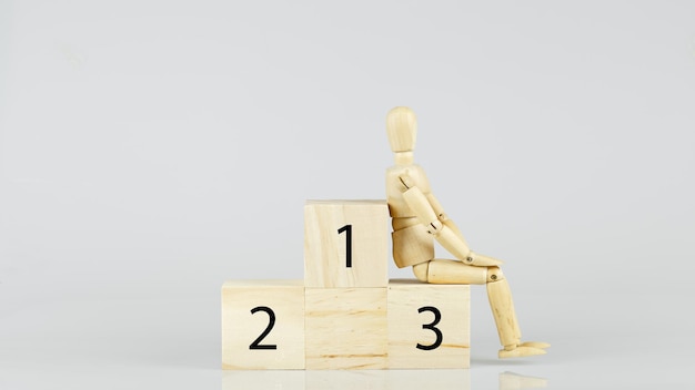 Wooden mannequin sitting 3rd place on podium blocks. âwhite background, goal objective destination. image size 16-9.