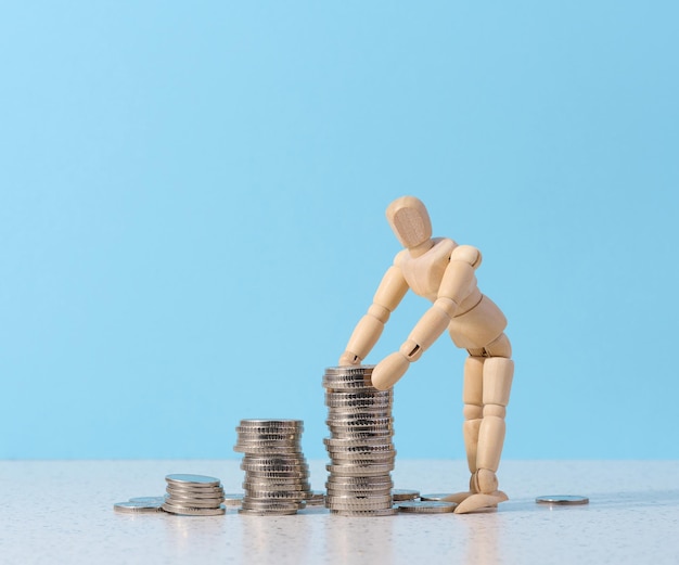 Wooden mannequin and a stack of coins on a blue background