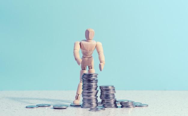 Wooden mannequin and a stack of coins on a blue background