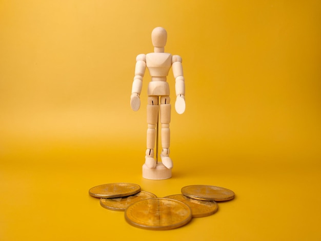 Wooden mannequin stand infront bitcoins on a yellow background