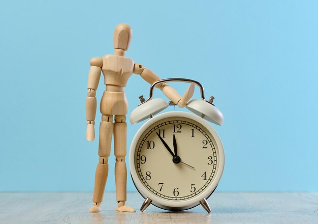 Wooden mannequin standing next to an alarm clock