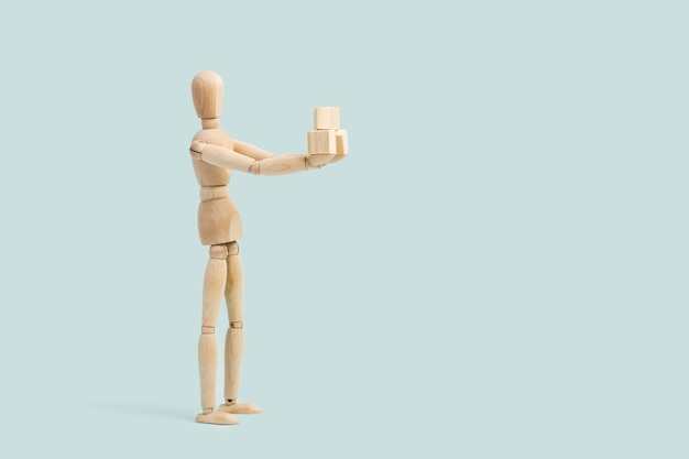 A wooden mannequin toy holding small wooden blocks