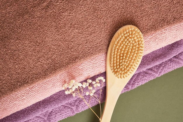 Wooden massage brush and Stack of bath towels on green wooden background closeup copy space