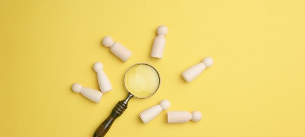 Wooden men and a magnifying glass on a yellow background. Recruitment concept, search for talented and capable employees, career growth, flat lay