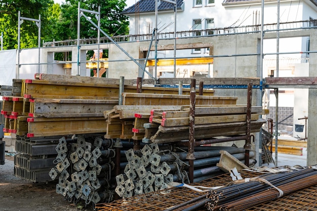 Wooden and metal beams stacked together with reinforcement lie against the backdrop of the walls of a house under construction