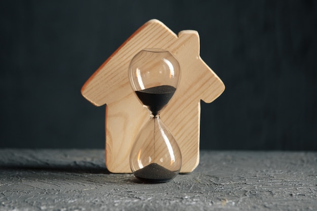 Wooden model of house and hourglass close-up. Saving and buying a property concept.