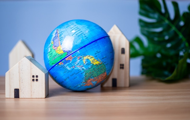 Photo a wooden model house is placed beside a replica globe. placed on a wooden table with a light gray background. save world concept