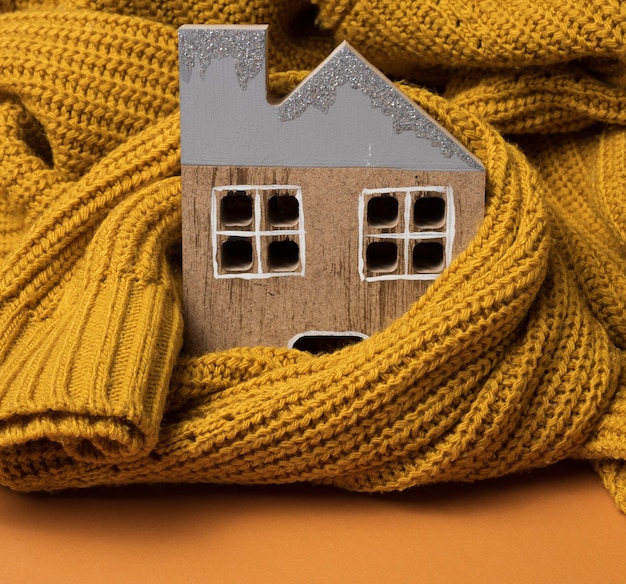 Foto il modello in legno della casa è avvolto in un caldo maglione lavorato a maglia. concetto di prestito per l'isolamento della casa, energia alternativa