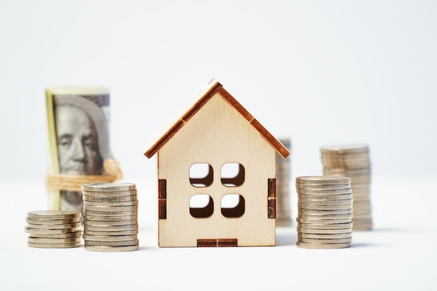 Wooden model of a house with a stack of coins and money on a white background