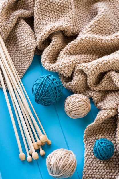 Wooden needles lie next to the bright tangle of threads and knitted blanket on blue background