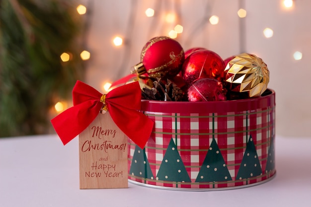 Una nota di legno con fiocco rosso e testo buon natale e felice anno nuovo una scatola di latta rotonda con palline giocattolo