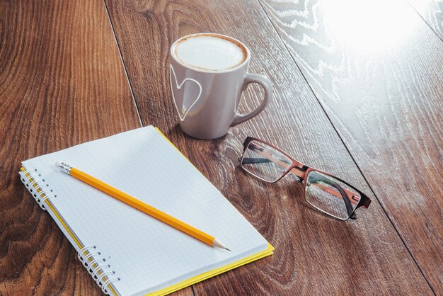 On wooden  notebook pencil, coffee and flowers.