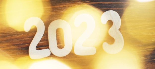 Wooden number 2023 on christmas beautifull shiny gold background sparkle festive blurred bokeh