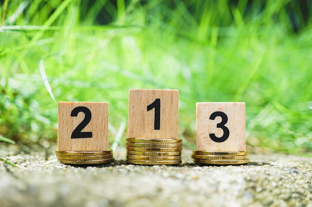 Wooden number on golden stack coins with green nature background 