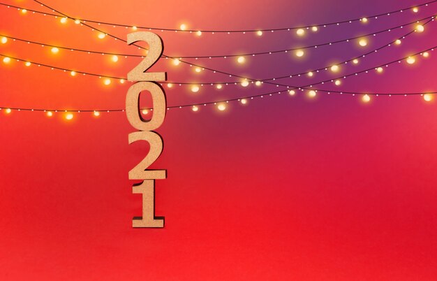 Wooden numbers in a New Year's cap on a red background with a luminous garland.