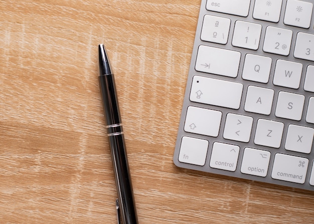 Wooden office table with keyboard and pen, top view with copy space