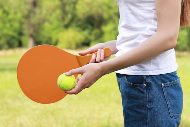 Photo a wooden paddle for playing tennis and a ball in the hands of a girl outdoor games closeup