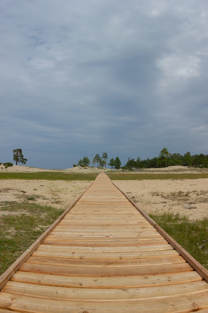 Wooden path stretching beyond the horizon surrounded by grass and sand on a cloudy day