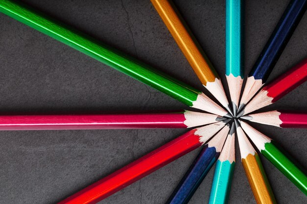 Wooden pencils of different colors in the shape of a star on a black background.