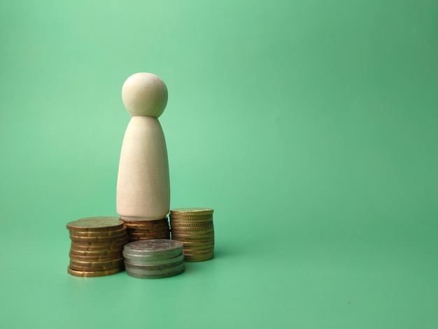 Wooden people figures and coins on a green background with copy\
space