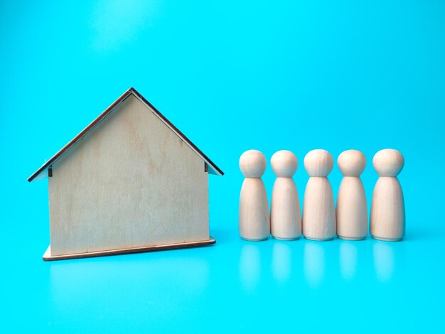 Wooden people figures and wooden house on blue background real\
estate concept