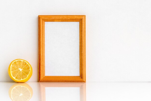 Wooden photo frame and lemon on white background Minimalistic gentle summer layout Blank for a postcard