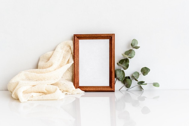 Wooden photo frame with a sprig of eucalyptus on a white wooden table Minimalistic delicate layout Blank for a postcard