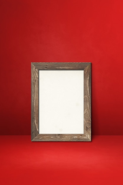 Wooden picture frame leaning on a red wall. Blank mockup template