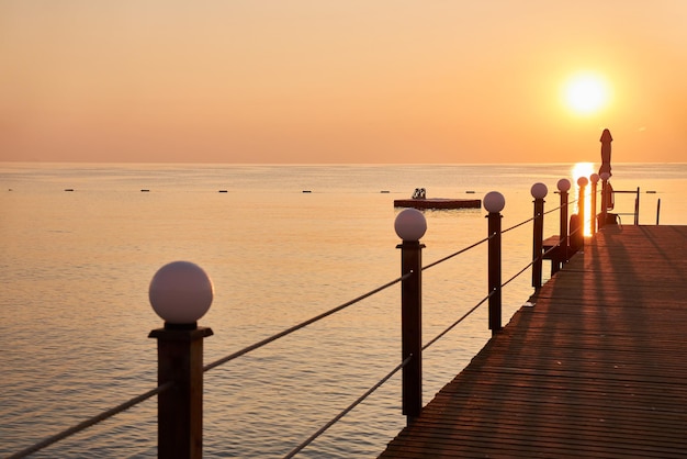 写真 オレンジ色の空と昇る太陽を背景にビーチの木製の桟橋