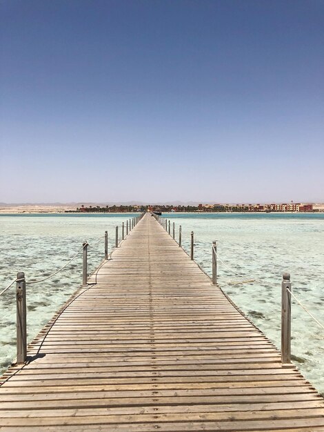 Wooden pier over sea against clear blue sky