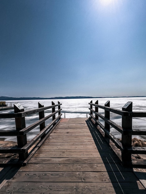 Foto un molo di legno con un cielo azzurro e ghiaccio sul fondo.