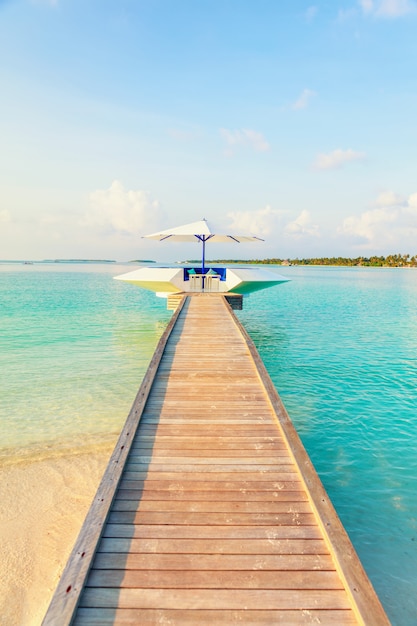 Wooden pier with small resting place by tropical blue sea, vertical composition