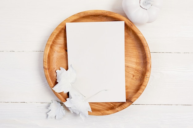 Wooden place with white sheet of paper. White pumpkin, berries and leaves