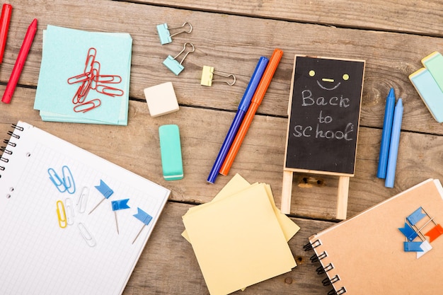 Wooden plaque with the inscription Back to school near notepads papers and other stationery on brown wooden table